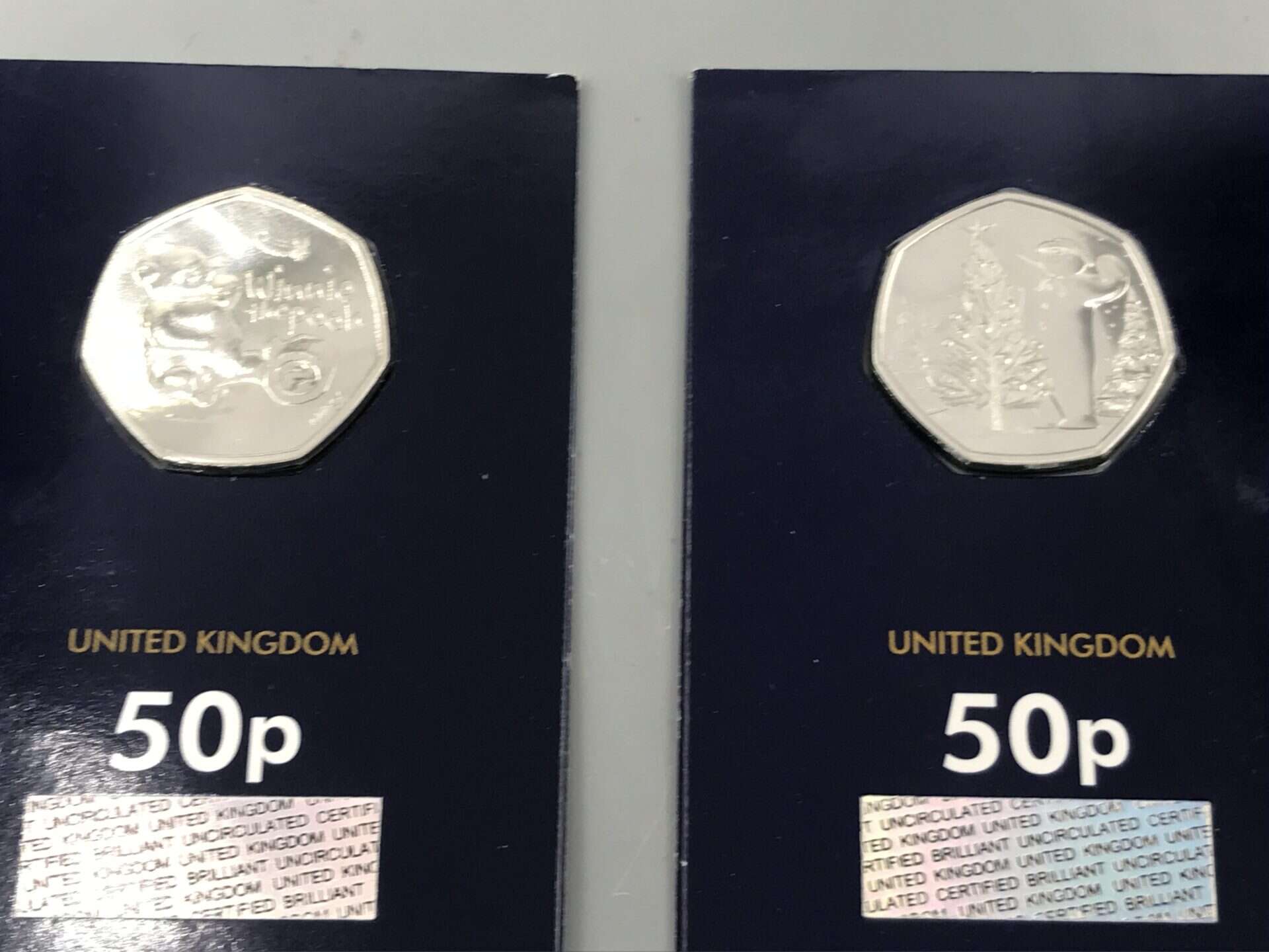 Two uncirculated United Kingdom 50p coins in official display cards, featuring themed designs including a bear character and Christmas tree scene