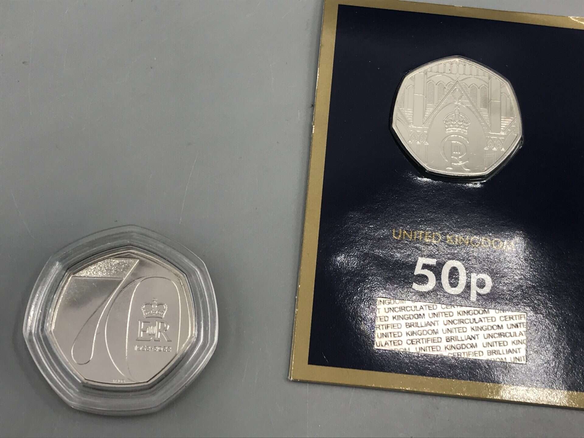Two UK 50p commemorative coins, one celebrating a royal jubilee in a capsule and one in official display card with crown and cathedral design