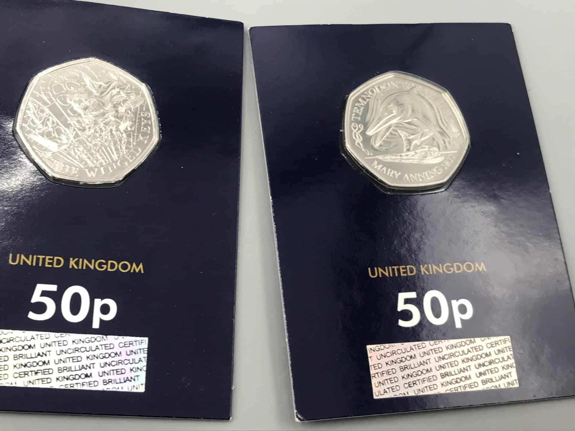 Two uncirculated UK 50p coins in display cards featuring prehistoric creatures including a winged dinosaur and a Temnodontosaurus from the Mary Anning series