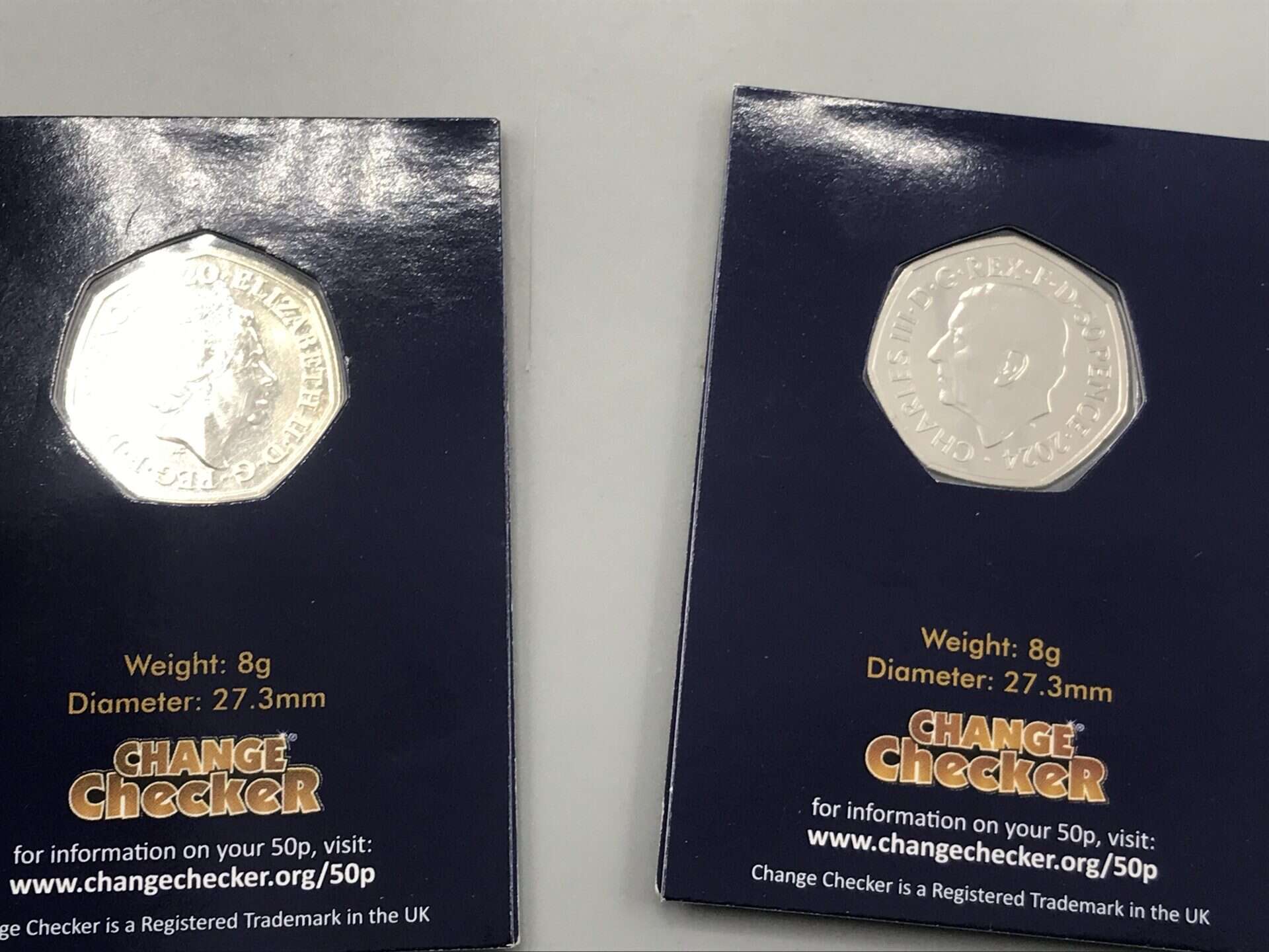 Two uncirculated UK 50p coins in Change Checker display cards showing obverse portraits of Queen Elizabeth II and King Charles III