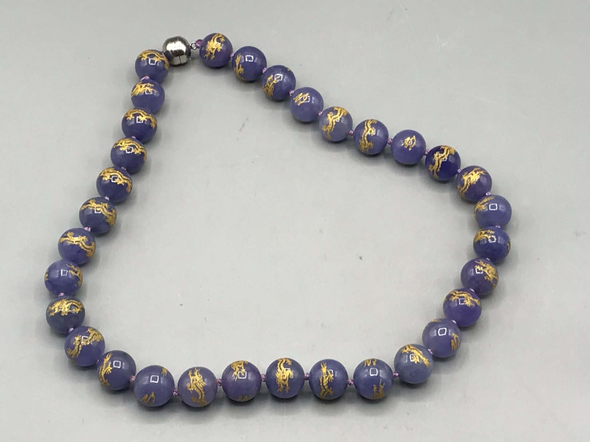Purple jade bead necklace with gold dragon motifs and metal clasp.