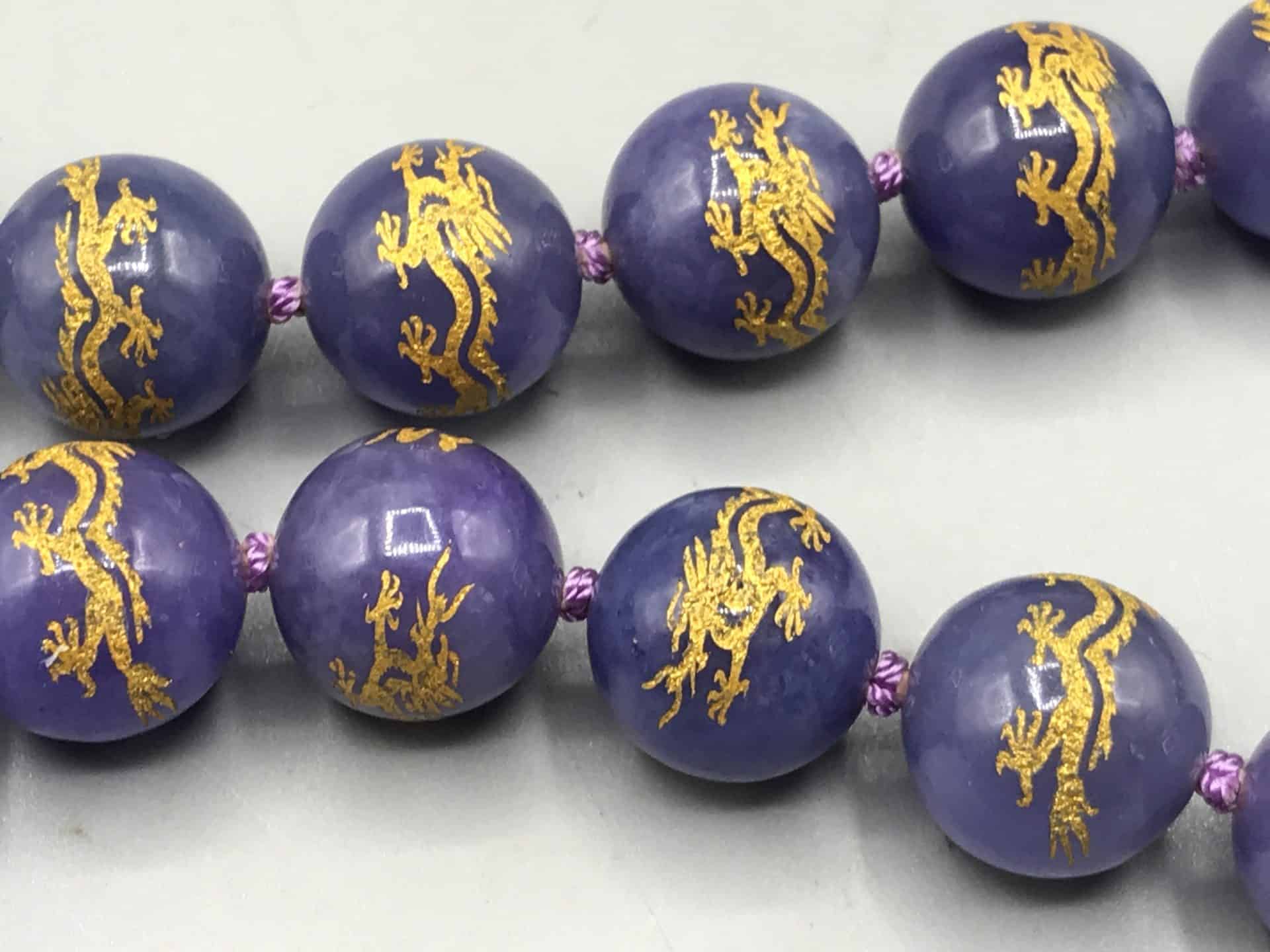 Close-up view of purple jade beads with gold dragon designs.