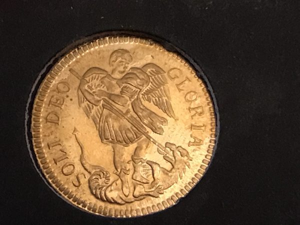 Close-up of a gold coin depicting St. Michael slaying a dragon with the inscription “SOLI DEO GLORIA” around the edge.