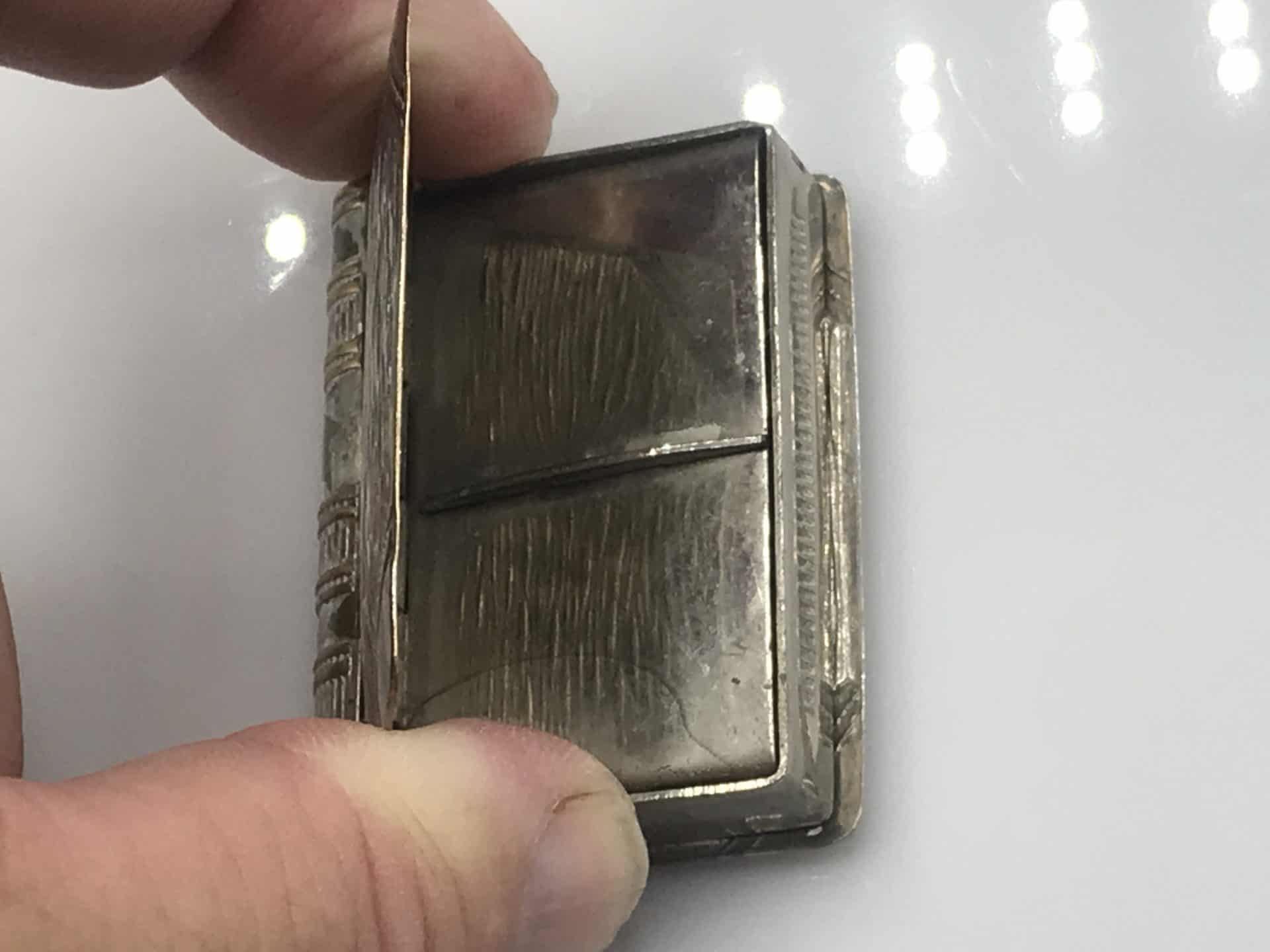 Close-up of an antique silver book-form vesta case with a hinged compartment open, revealing the interior designed to hold stamps.