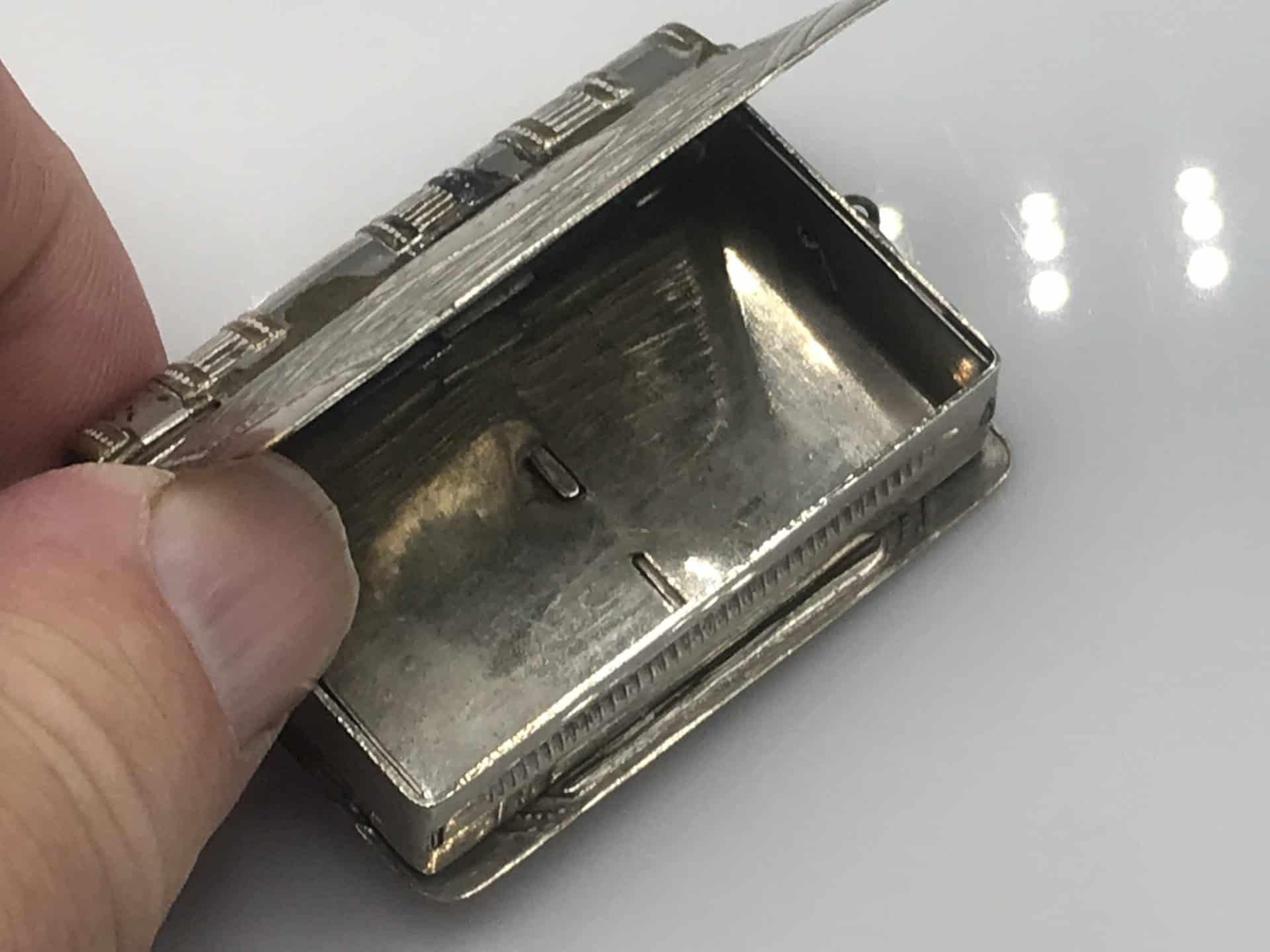 Open view of an antique silver plate book-form vesta case showing the interior compartment and hinged lid.