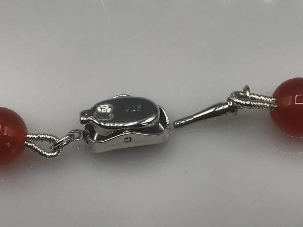 Close-up of a sterling silver clasp on a carnelian bead necklace, marked "925," with the clasp open and the connecting hook visible.