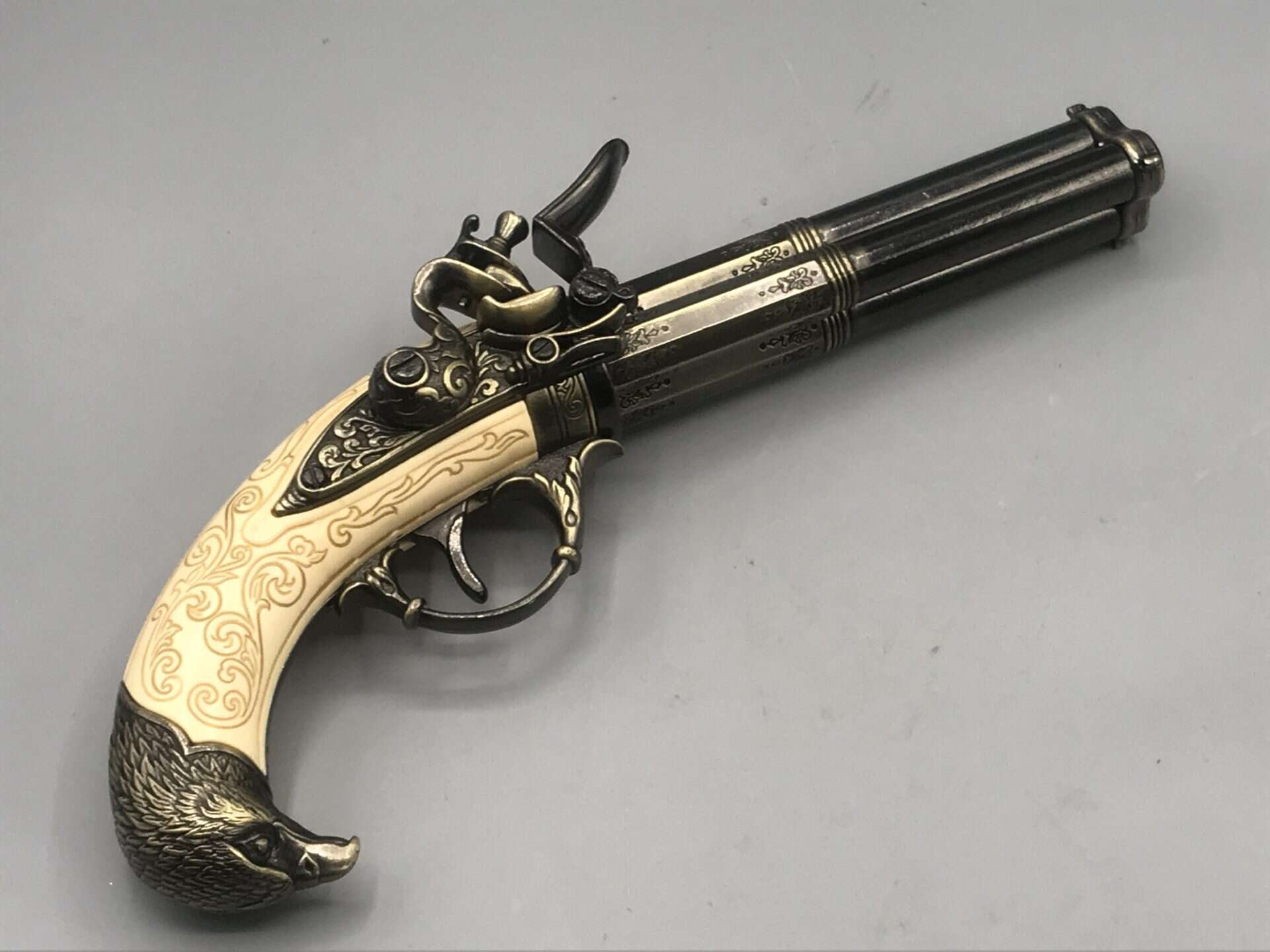 Replica 18th-century French flintlock pistol with three rotating barrels and ornate engraved grip.