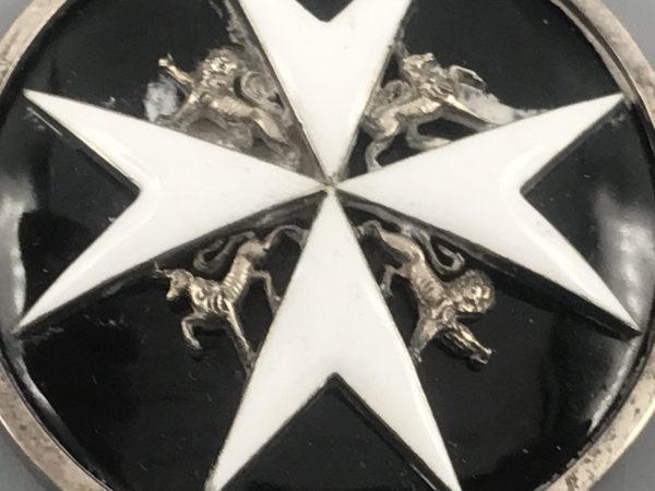 Close-up of the front of a St John Ambulance medal showing the white enamel Maltese cross and central heraldic lions and unicorns