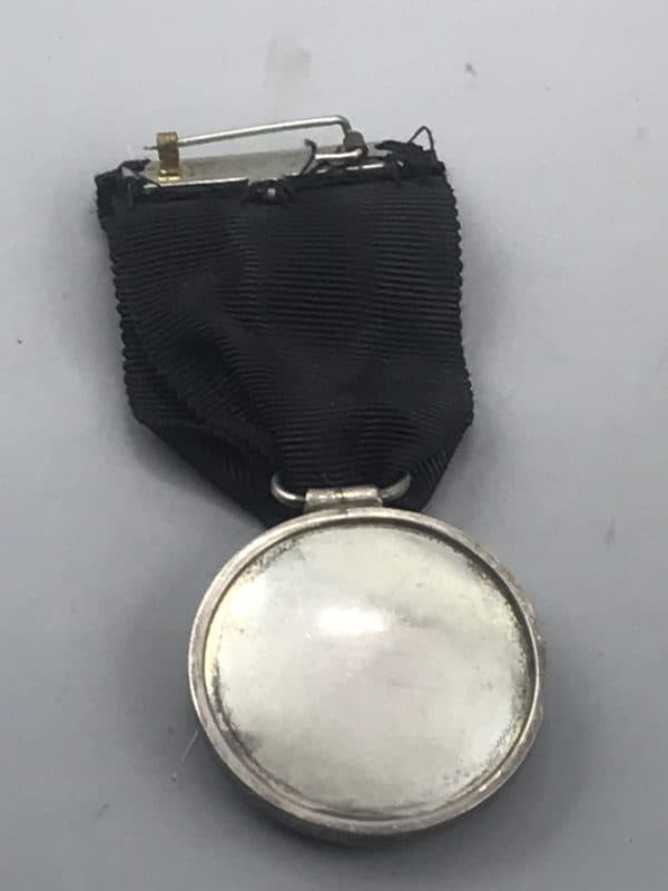 Back view of a St John Ambulance medal showing the plain silver reverse and mounting pin with black ribbon