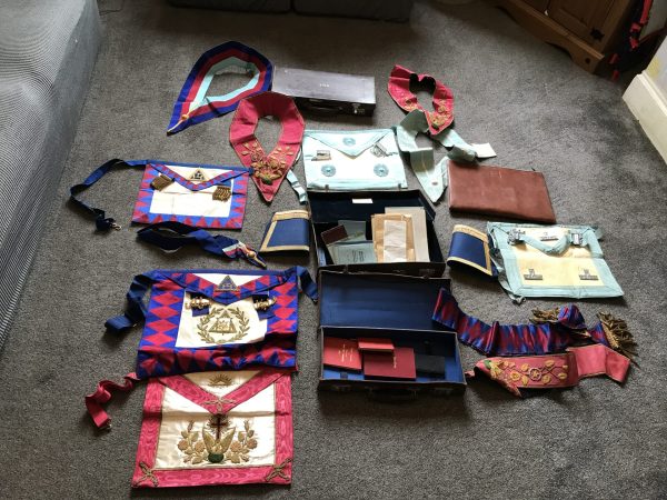 Collection of vintage Masonic regalia including aprons, sashes, collars, cuffs, and cases laid out on carpeted floor
