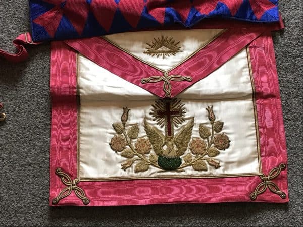 Close-up of a vintage Masonic apron with embroidered cross, rose, and all-seeing eye symbols