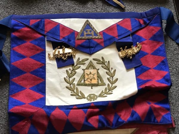Close-up of vintage Masonic apron with red and blue triangle border and embroidered Masonic symbols