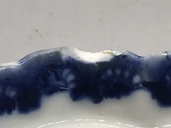 Close-up of rim chip on 18th century Chinese export porcelain dish from the Qianlong period, showing underglaze cobalt blue border decoration