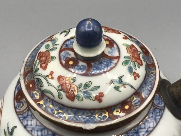 Close-up of domed lid from 18th century Kangxi Chinese porcelain teapot with floral famille verte decoration and blue knop finial