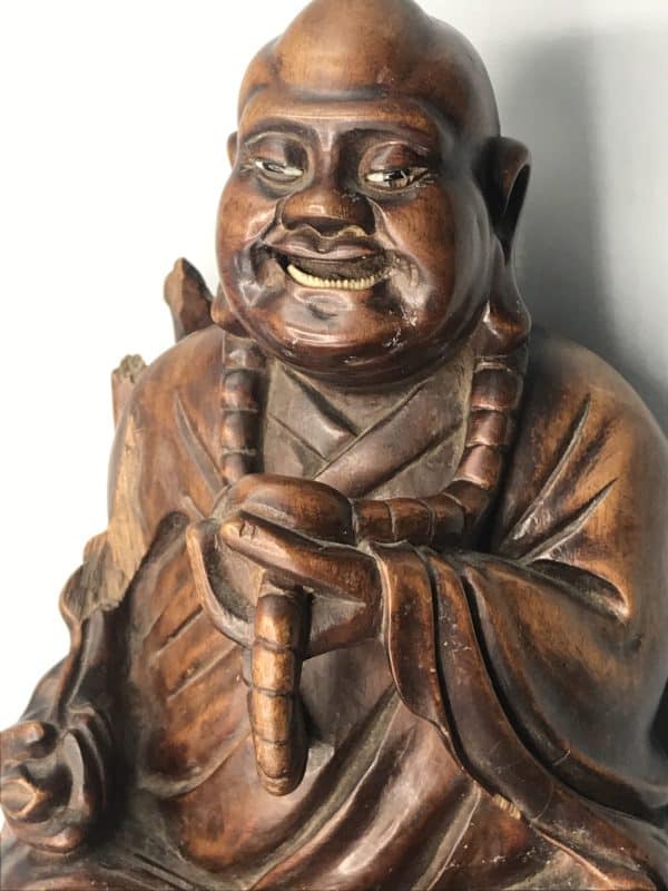 Close-up of antique Chinese carved hardwood Buddha statue, top half view showing Budai’s smiling face, prayer beads, and robe detail