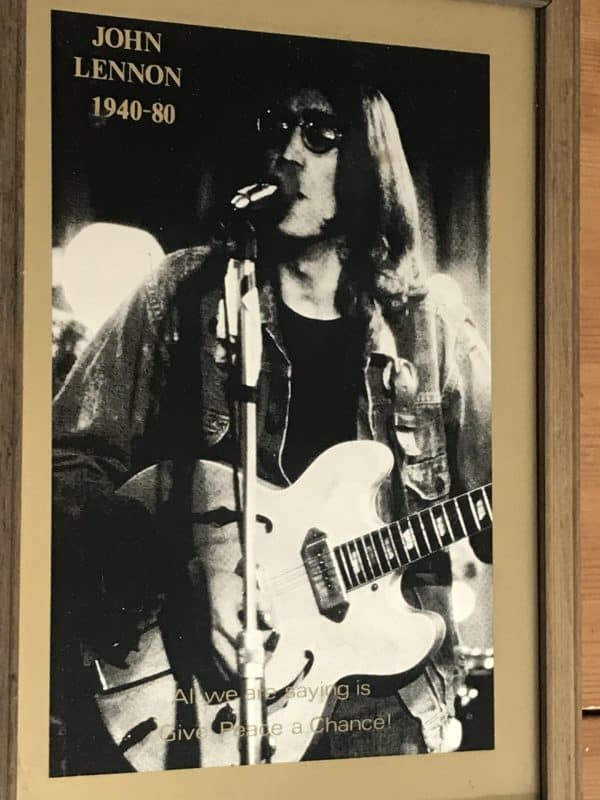 Full close-up of 1980s John Lennon memorial mirror without frame, showing monochrome portrait with guitar and printed peace quote