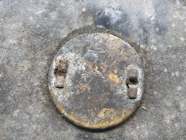 Close-up of worn brass identification disc on lid of early 20th century mining explosives canister, showing corrosion and patina