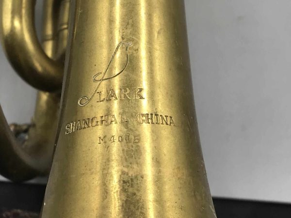 Close-up of maker’s mark on vintage brass cornet by Lark Shanghai China, showing engraved logo and serial number