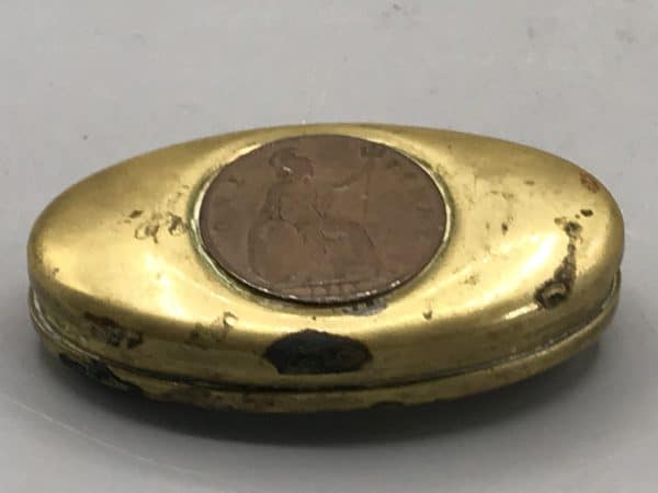 Close-up of an antique brass snuff box with inset 1916 copper penny on the lid, showing surface wear and patina.