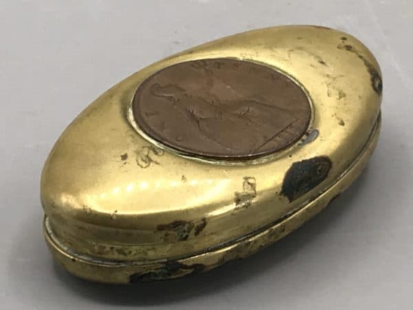 Side view of antique brass snuff box showing inset 1916 penny and worn patina along the edges.