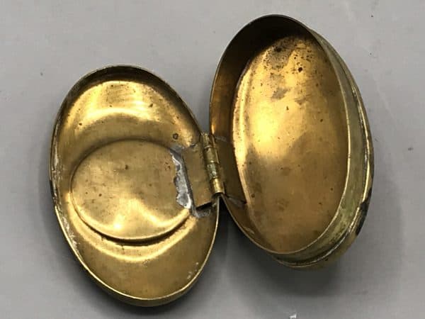 Interior view of antique brass snuff box shown open, displaying hinge and inner compartments.