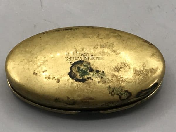 Underside of antique brass snuff box showing "Made in Wales" stamp and age-related oxidation.