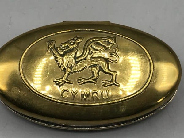 Close-up of brass snuff box lid featuring a raised Welsh dragon and “CYMRU” text.
