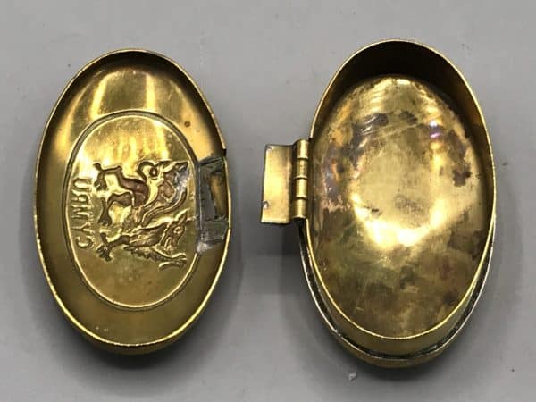 Interior view of modern brass snuff box showing detached lid with Welsh dragon and "CYMRU" motif.