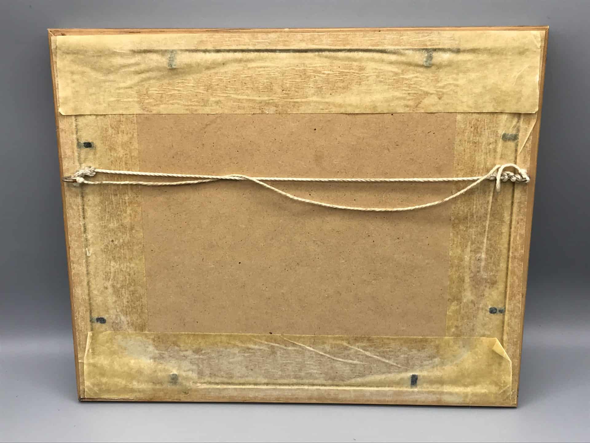 Back of framed watercolour winter village signed “Tom Menard,” showing MDF backing, old frame tape and hanging cord; frame 12 × 10 inches