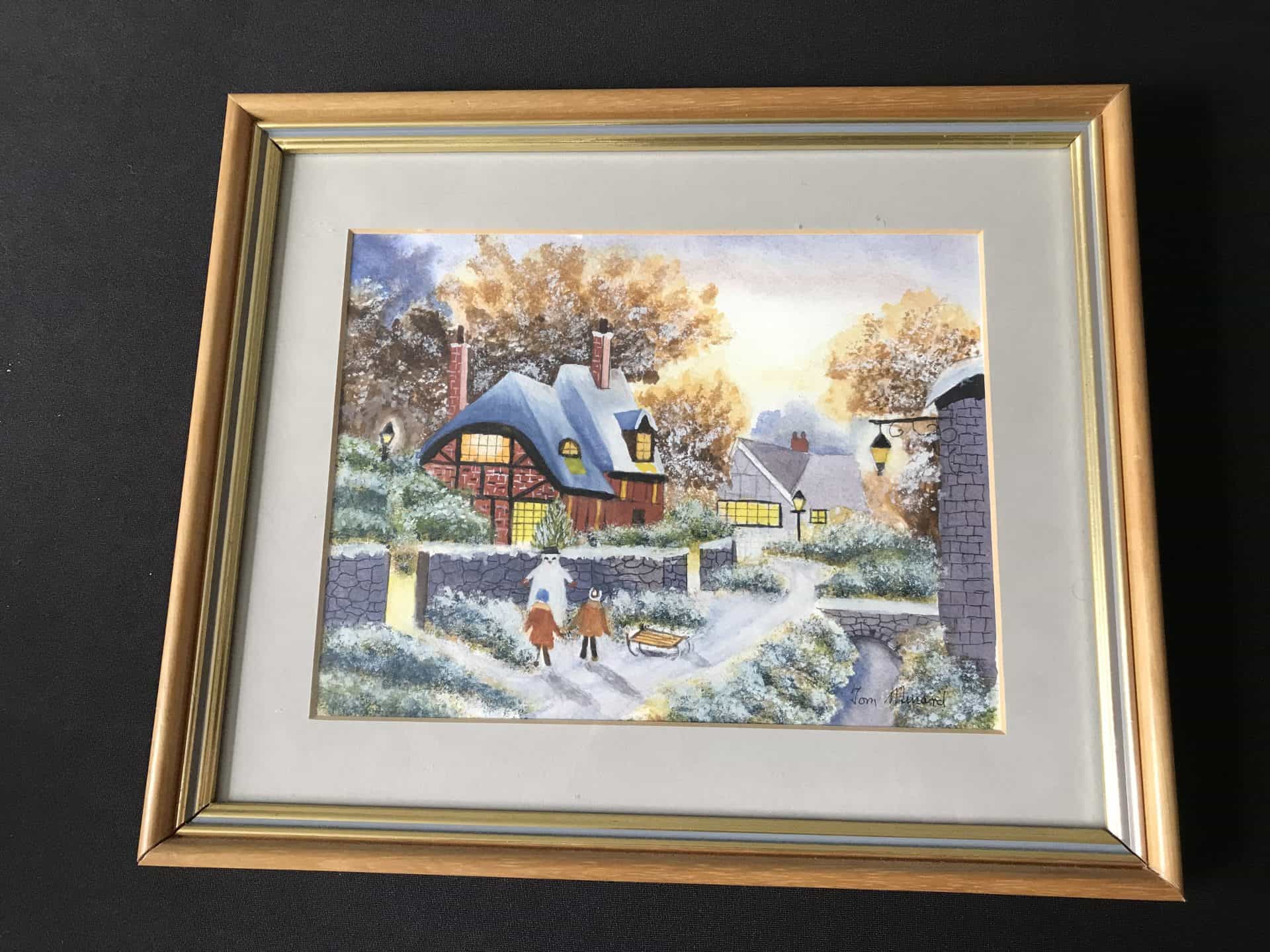 Framed watercolour of an English village snow scene with two children and a sledge, lamplight and stone bridge, signed “Tom Menard”; frame 12 × 10 inches