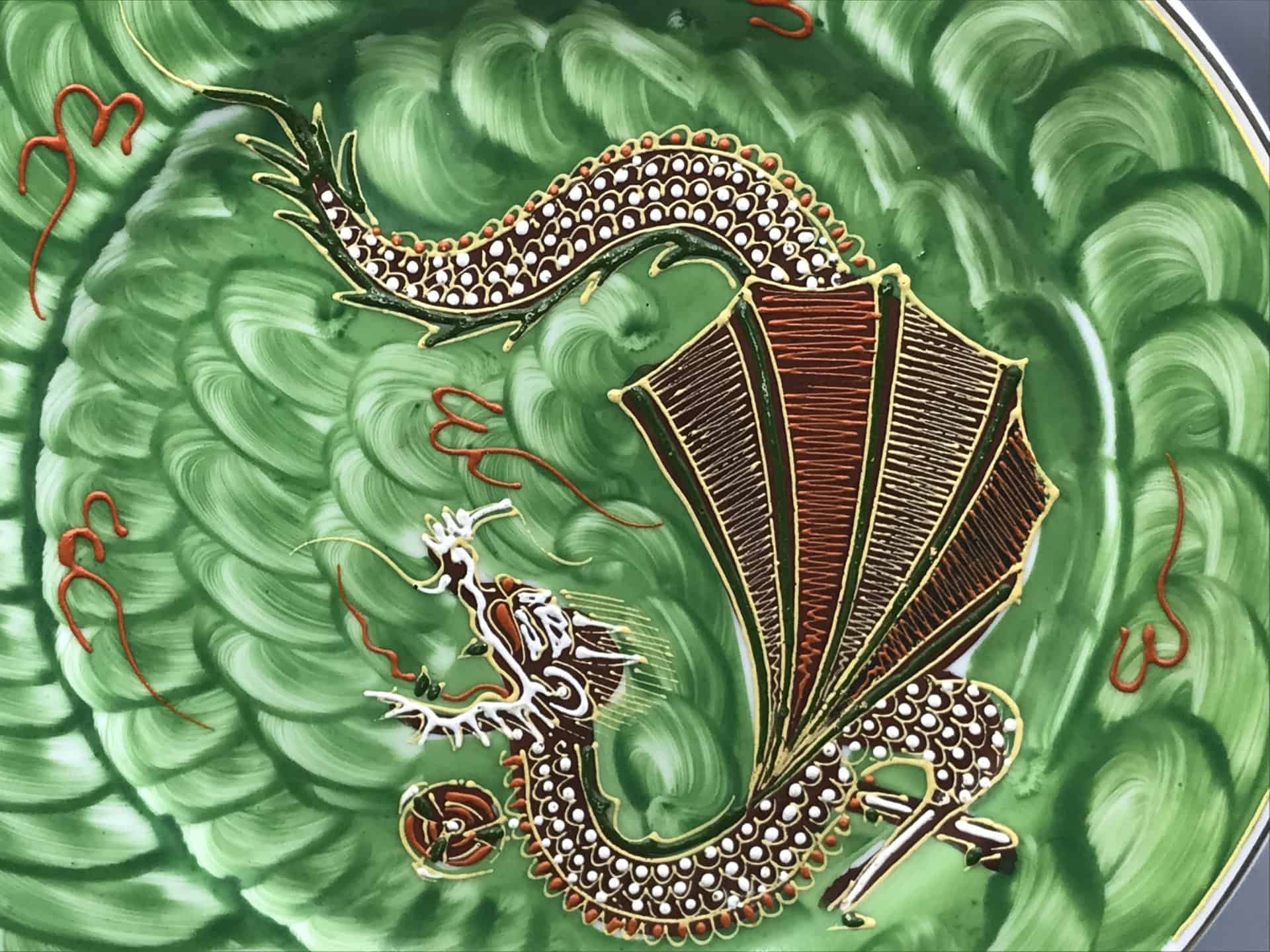 Close-up of raised moriage dragon on vintage Japanese porcelain plate with green swirl background