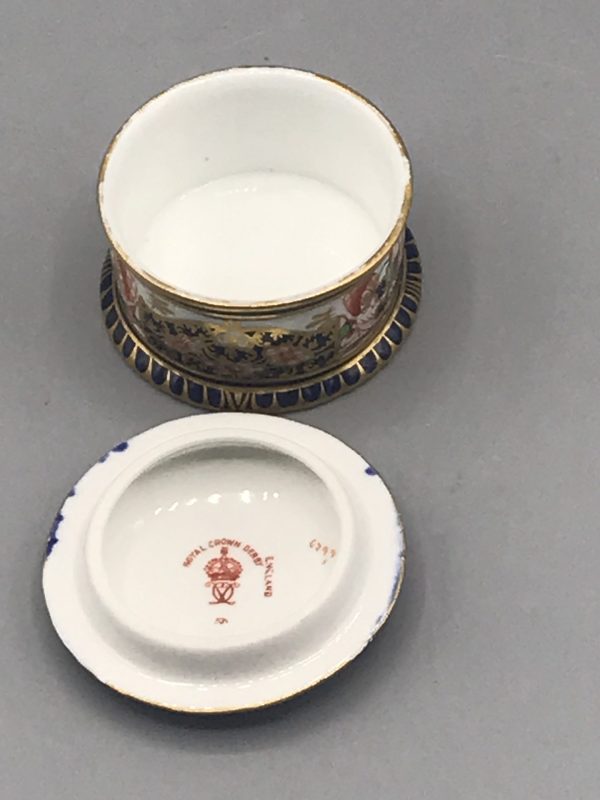 Royal Crown Derby Imari porcelain trinket pot with lid shown upside down in front, revealing interior and underside mark