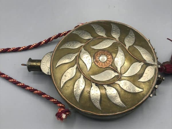 Close-up of antique Moroccan brass cantimplora flask with silver and copper inlay, showing detailed floral and leaf motif