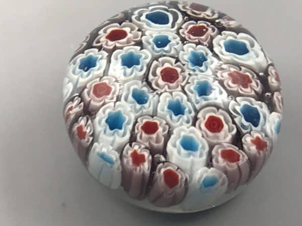 Top-down view of a mid-20th century Chinese millefiori glass paperweight showing densely packed floral glass canes in red, white, and blue beneath clear glass