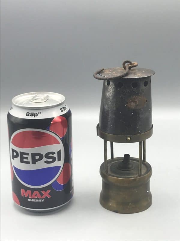 Antique brass and steel coal miner’s midget safety lamp displayed beside a Pepsi can for size comparison, showing its compact 6-inch height and aged patina.