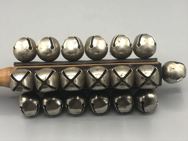 Close-up of vintage Dixon sleigh bells showing twin rows of metal bells with aged patina and secure mounting on a wooden frame.