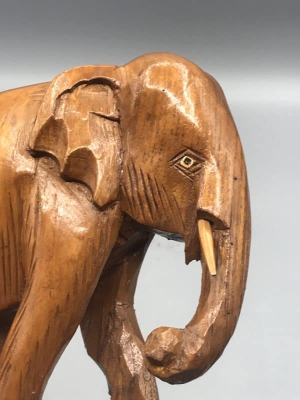 Close-up of antique hand-carved wooden elephant head, early 20th century, showing fine detail, inset eyes, and carved tusks.