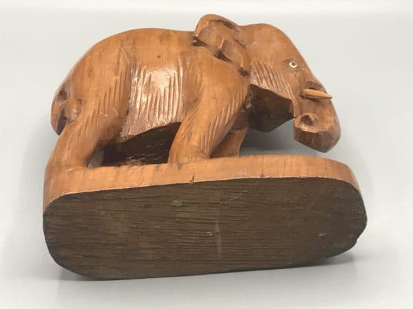 Antique hand-carved wooden elephant figurine shown on its side, displaying the carved underside and base details.