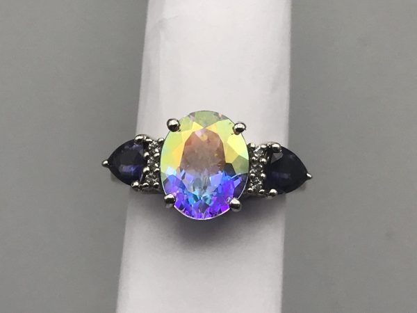 Front view of sterling silver TGGC ring featuring a large oval mystic quartz gemstone with rainbow iridescence, flanked by two pear-cut blue stones.