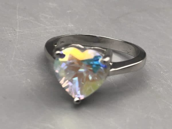 Close-up of sterling silver TGGC ring with iridescent heart-cut gemstone showing the maker’s mark “TGGC” stamped inside the band.