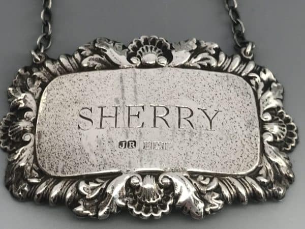 Close-up of sterling silver sherry decanter label by John Rose, Birmingham 1968, showing engraved title and rococo border, measuring 60mm by 40mm.