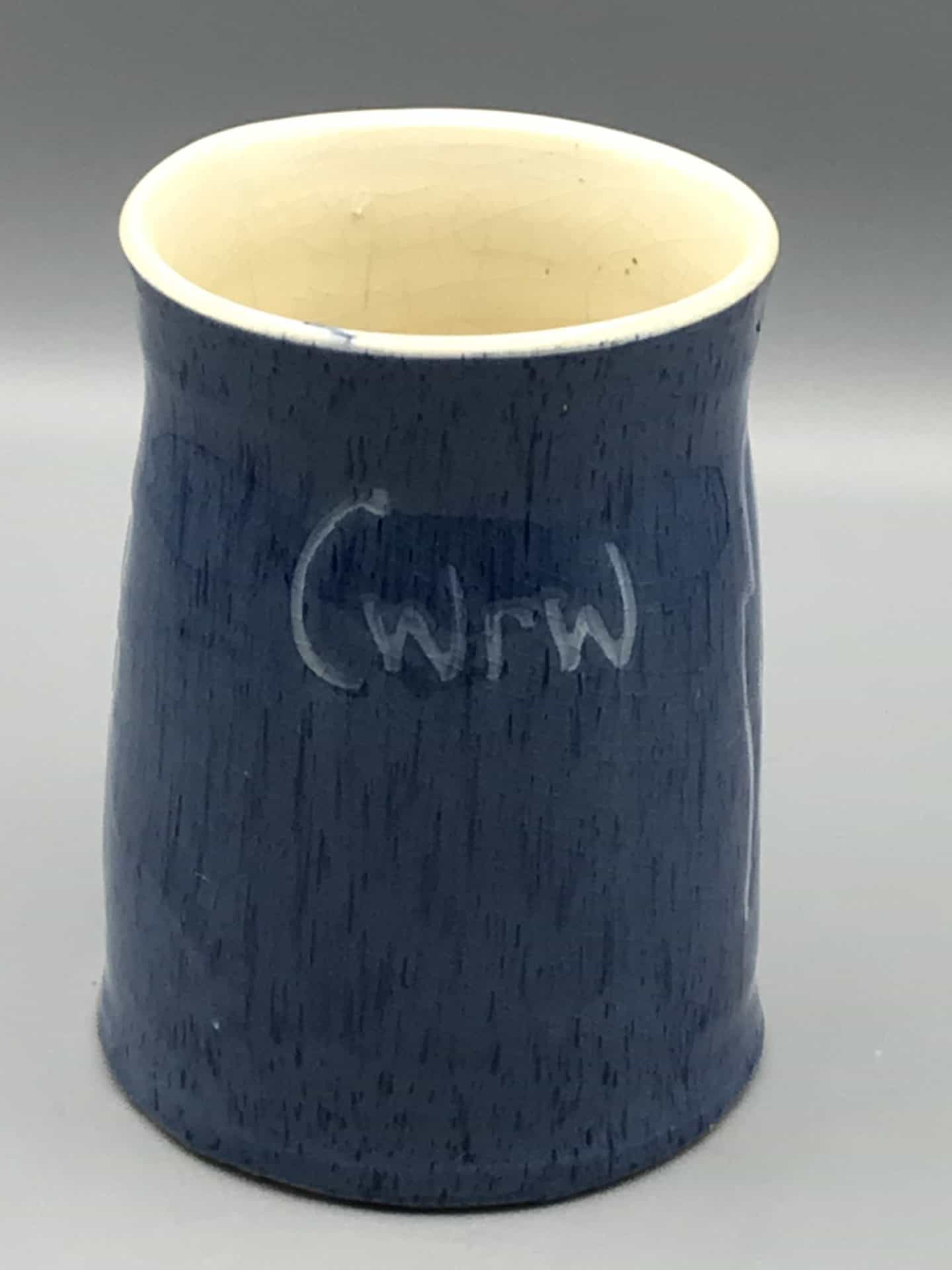 Front view of blue stoneware tankard by Claypits Pottery Ewenny, showing the word “cwrw” in lighter glaze and cream interior.