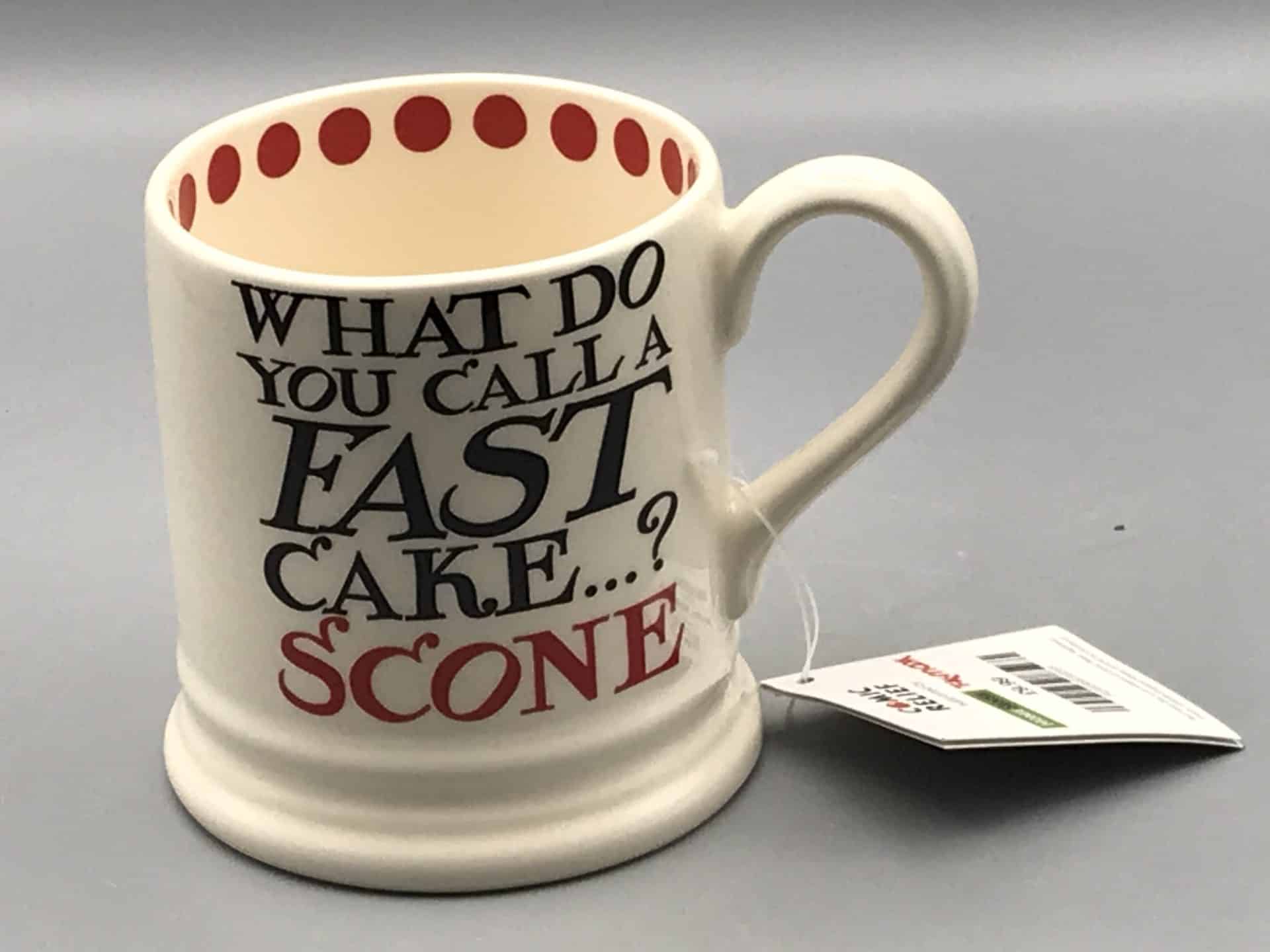 Emma Bridgewater pottery mug for Comic Relief with the phrase “What do you call a fast cake…? SCONE” in black and red lettering, cream body, and red polka dots inside rim.