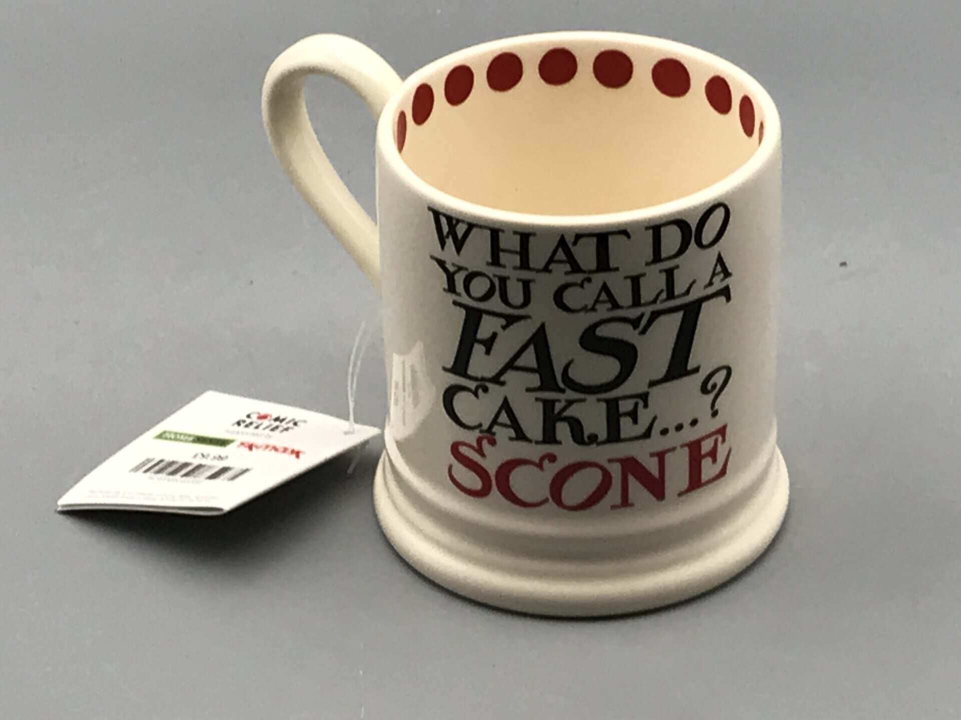 Emma Bridgewater Comic Relief mug with red interior polka dots and slogan “What do you call a fast cake…? SCONE,” shown with original tag.