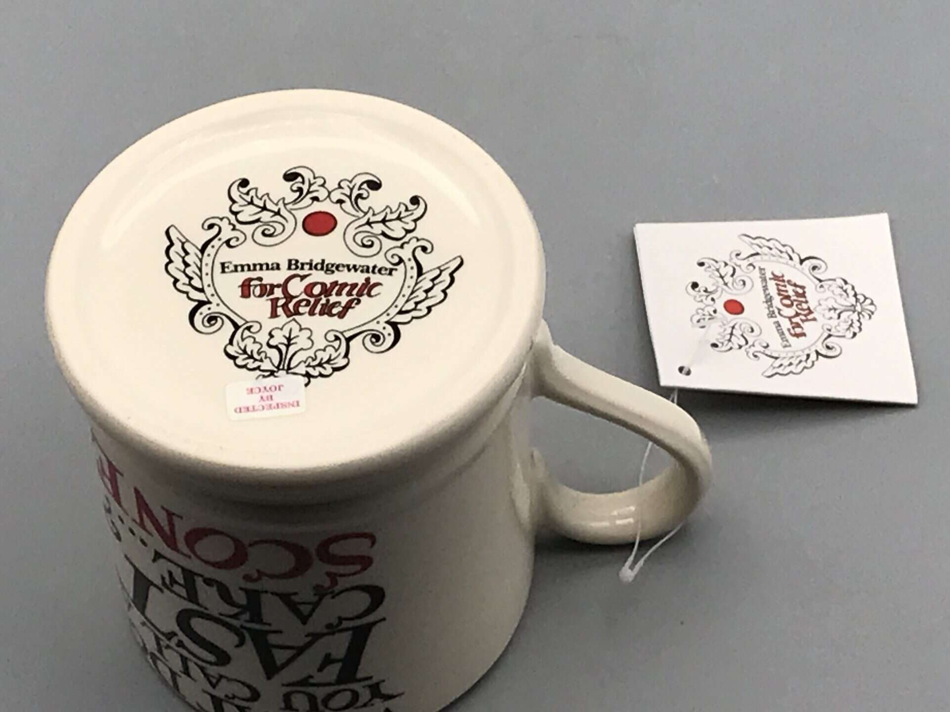 Base of Emma Bridgewater Comic Relief mug showing maker’s mark and decorative logo with red dot, accompanied by original swing tag.