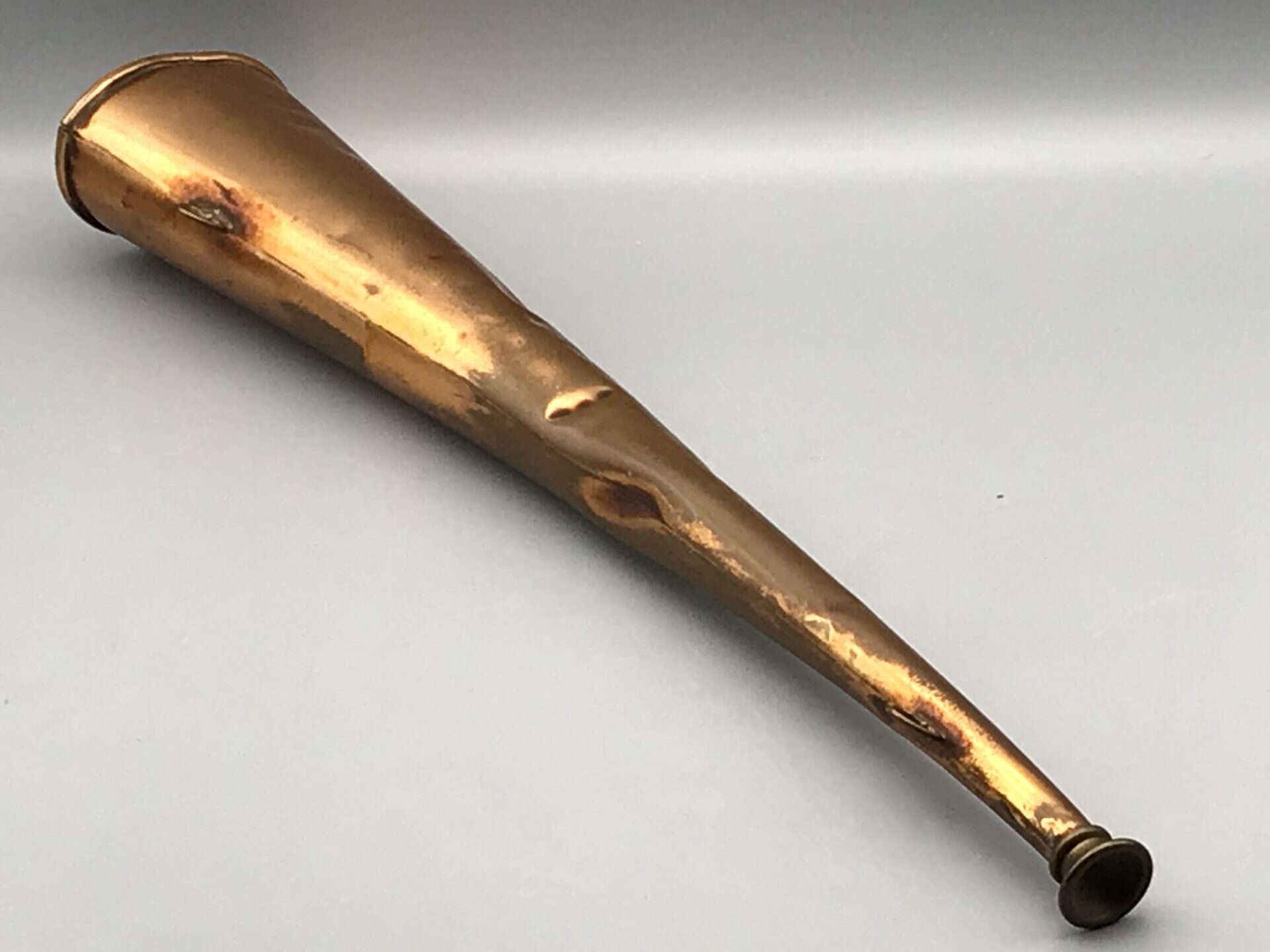 Antique copper hunting horn showing full length and surface dents with natural patina.