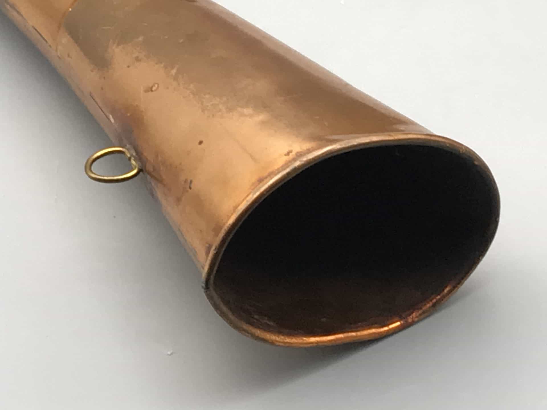 Close-up of the flared bell on an antique copper hunting horn with brass ring fitting and aged patina.
