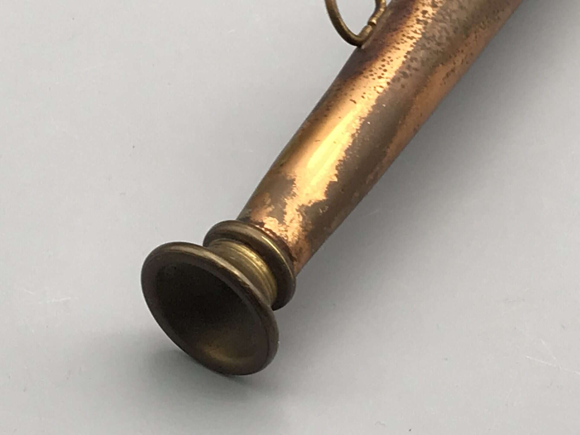 Close-up of the brass mouthpiece and copper body on an antique hunting horn showing aged surface and patina.