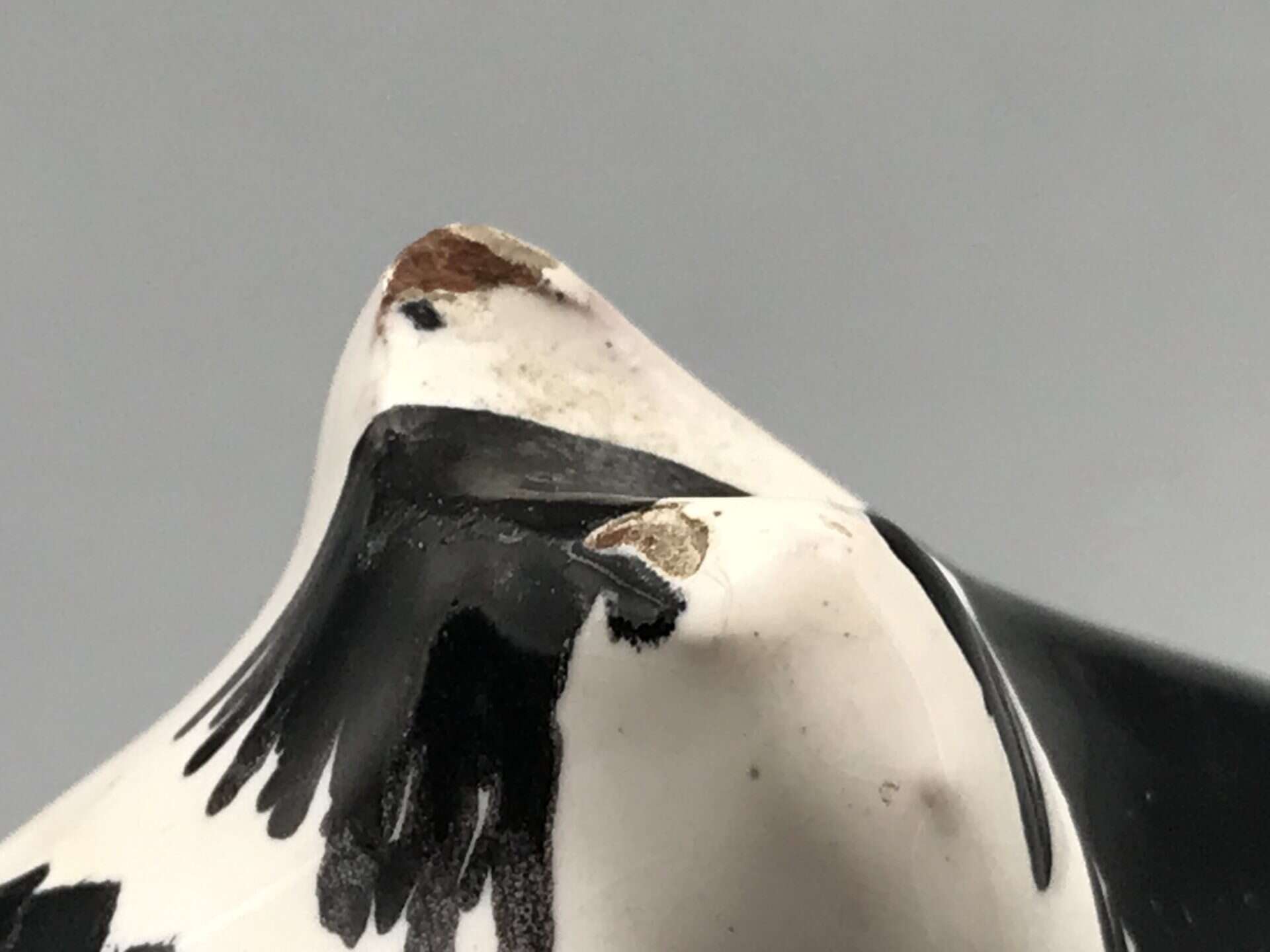 Close-up of a ceramic cow figurine showing black and white patterns with minor wear on the surface.