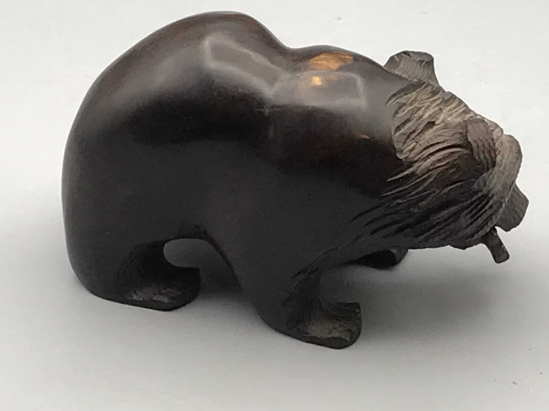 Side view of a hand-carved hardwood bear in Kibori Kuma style, holding a fish in its mouth.
